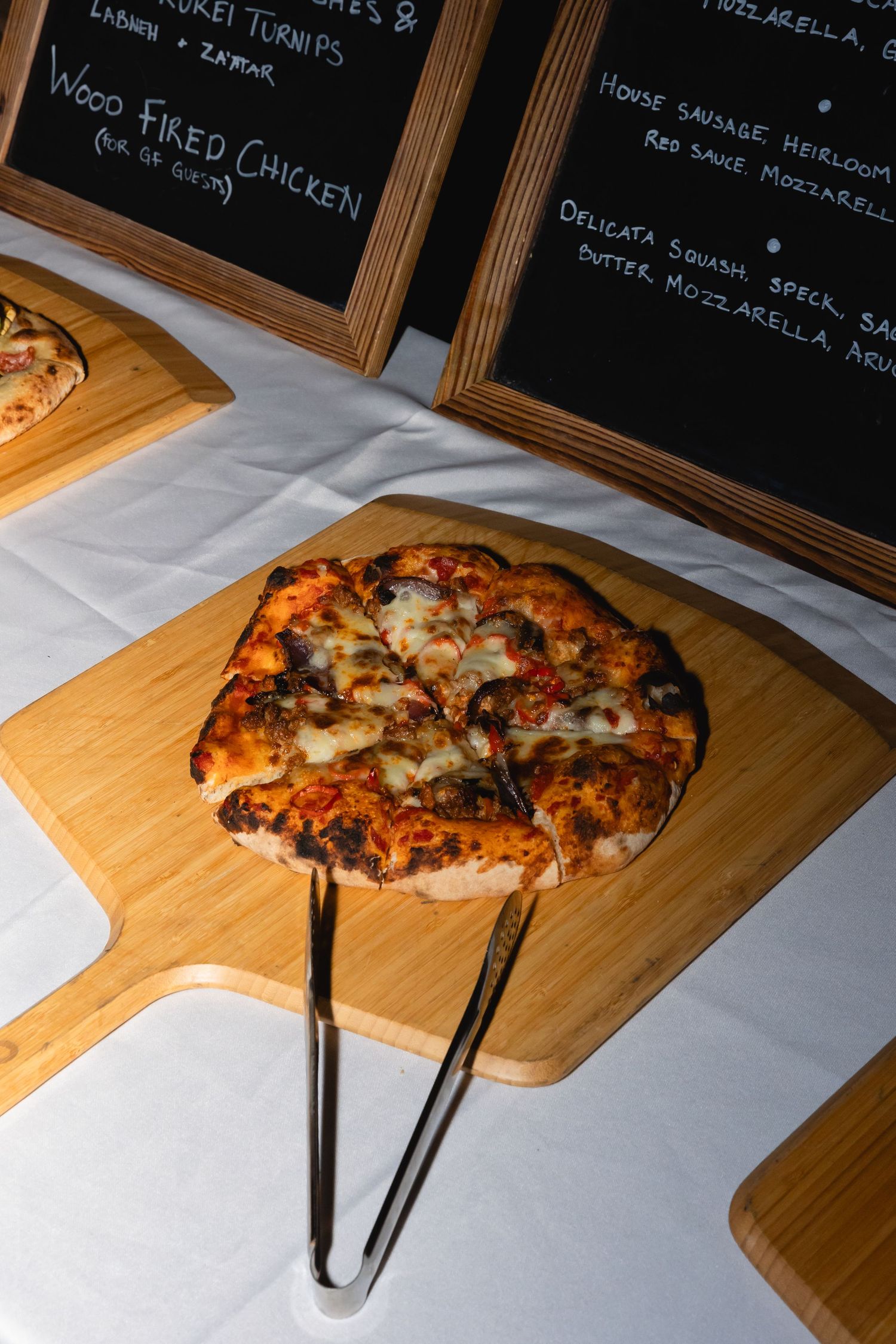 Homemade pizza with melted cheese served on a wooden cutting board with chalkboard menus in the background.