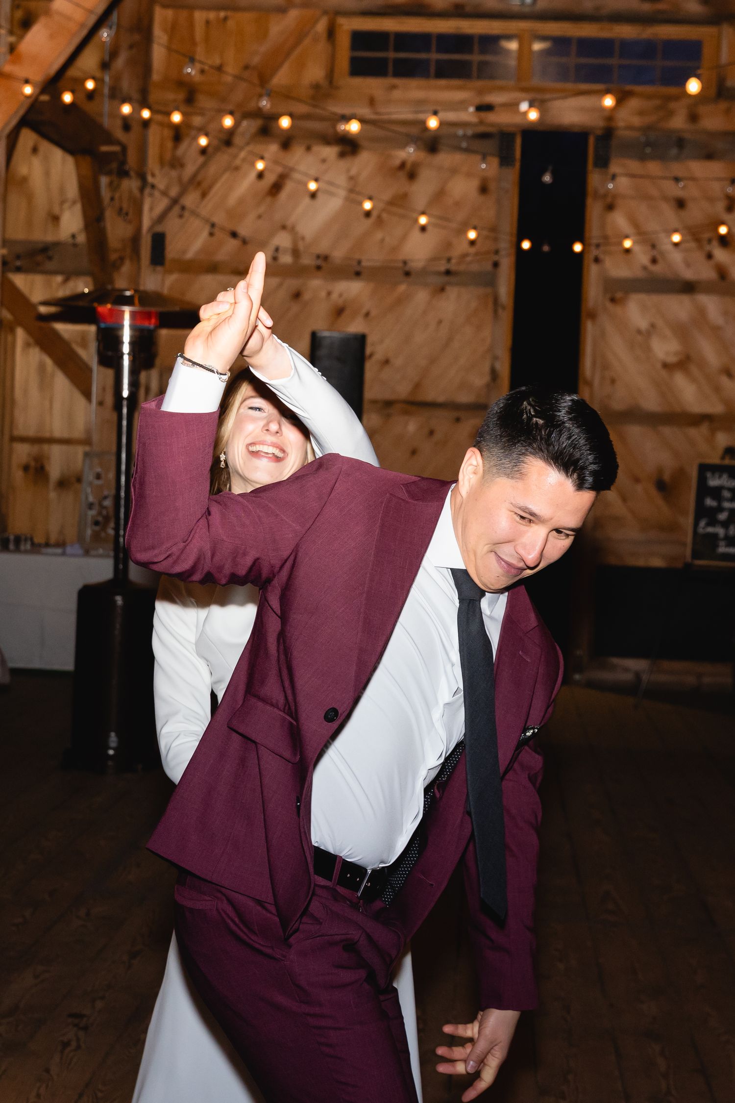Guests dancing and celebrating at a rustic barn wedding reception with string lights overhead.