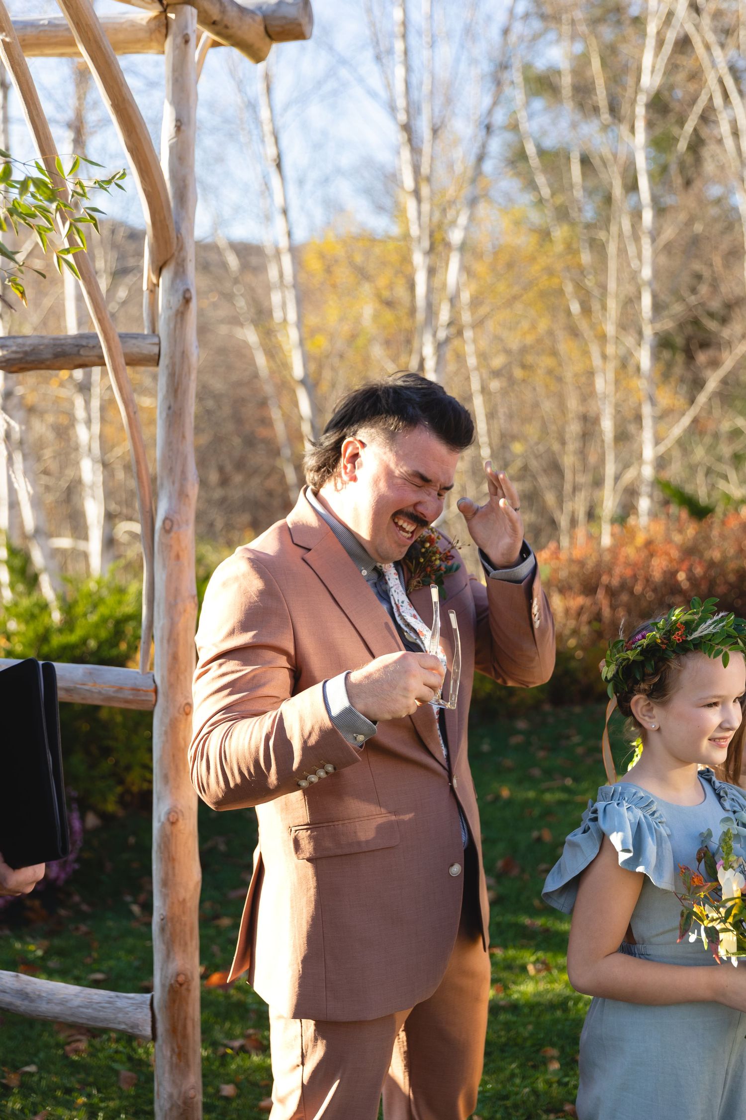 Emotional moment during outdoor wedding ceremony beneath wooden arch with fall foliage.