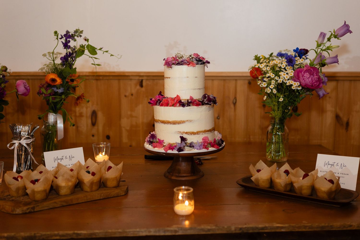 Three-tiered white wedding cake decorated with berries and flowers on display with desserts.