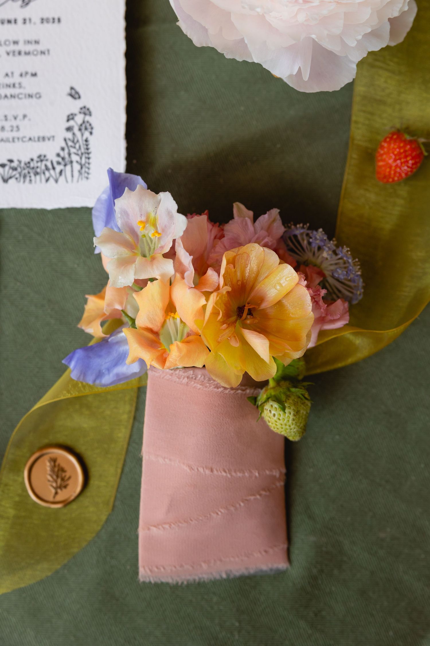 Pink and orange flowers arranged in a delicate display with green leaves on a dark surface.