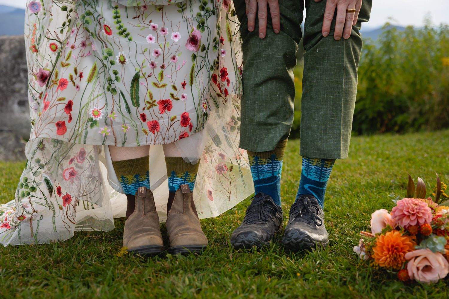 Feet of wedding guests standing in a row on grass with floral decor and autumn flowers visible.
