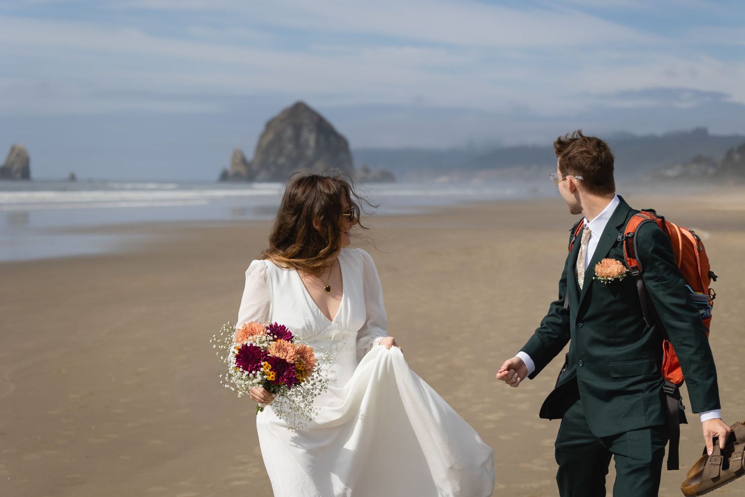 Couple walking along misty Cannon Beach with Haystack Rock visible in the background on their wedding day.