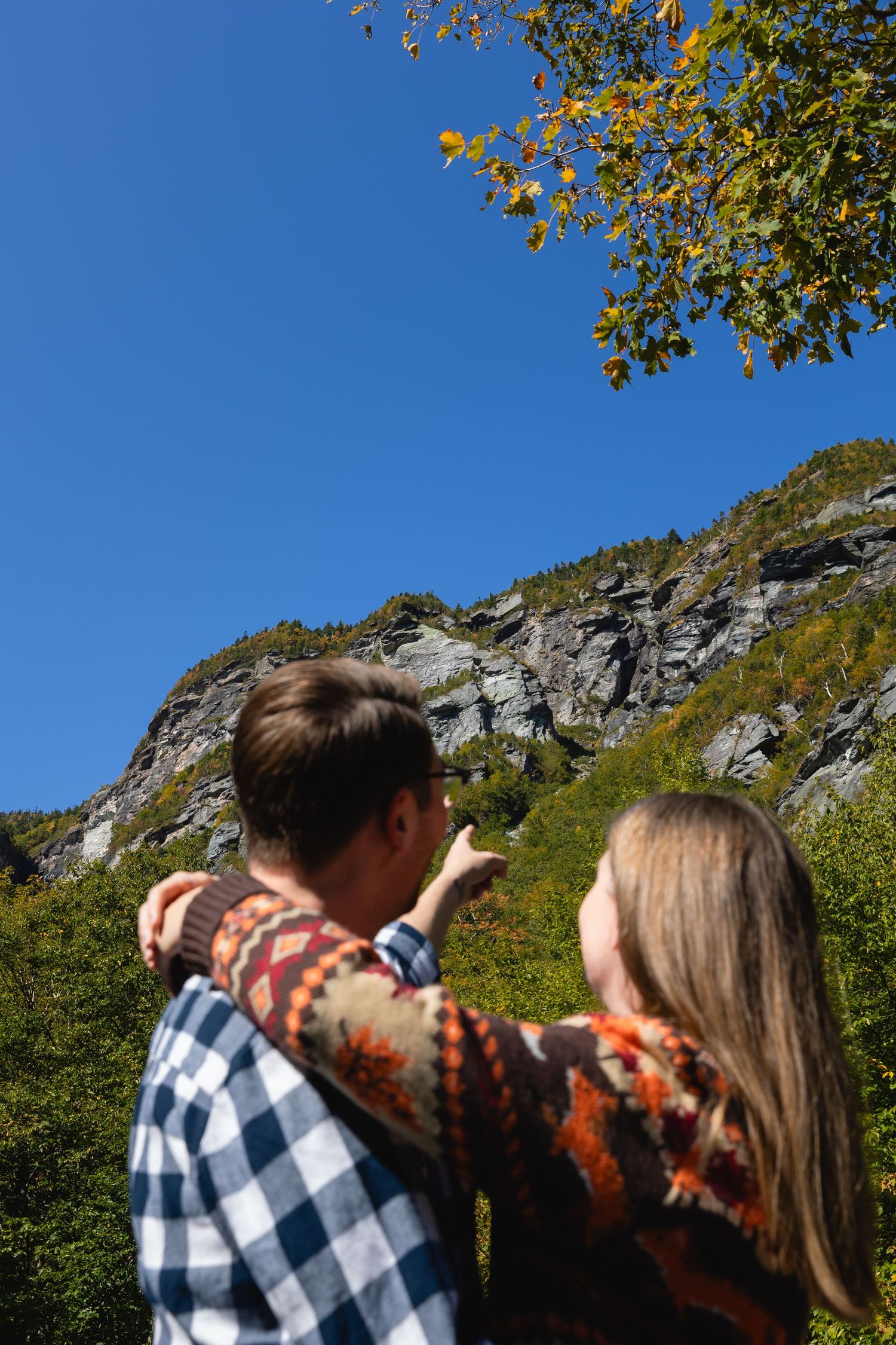 Couple looking up at a rocky mountain cliff face surrounded by colorful autumn foliage.