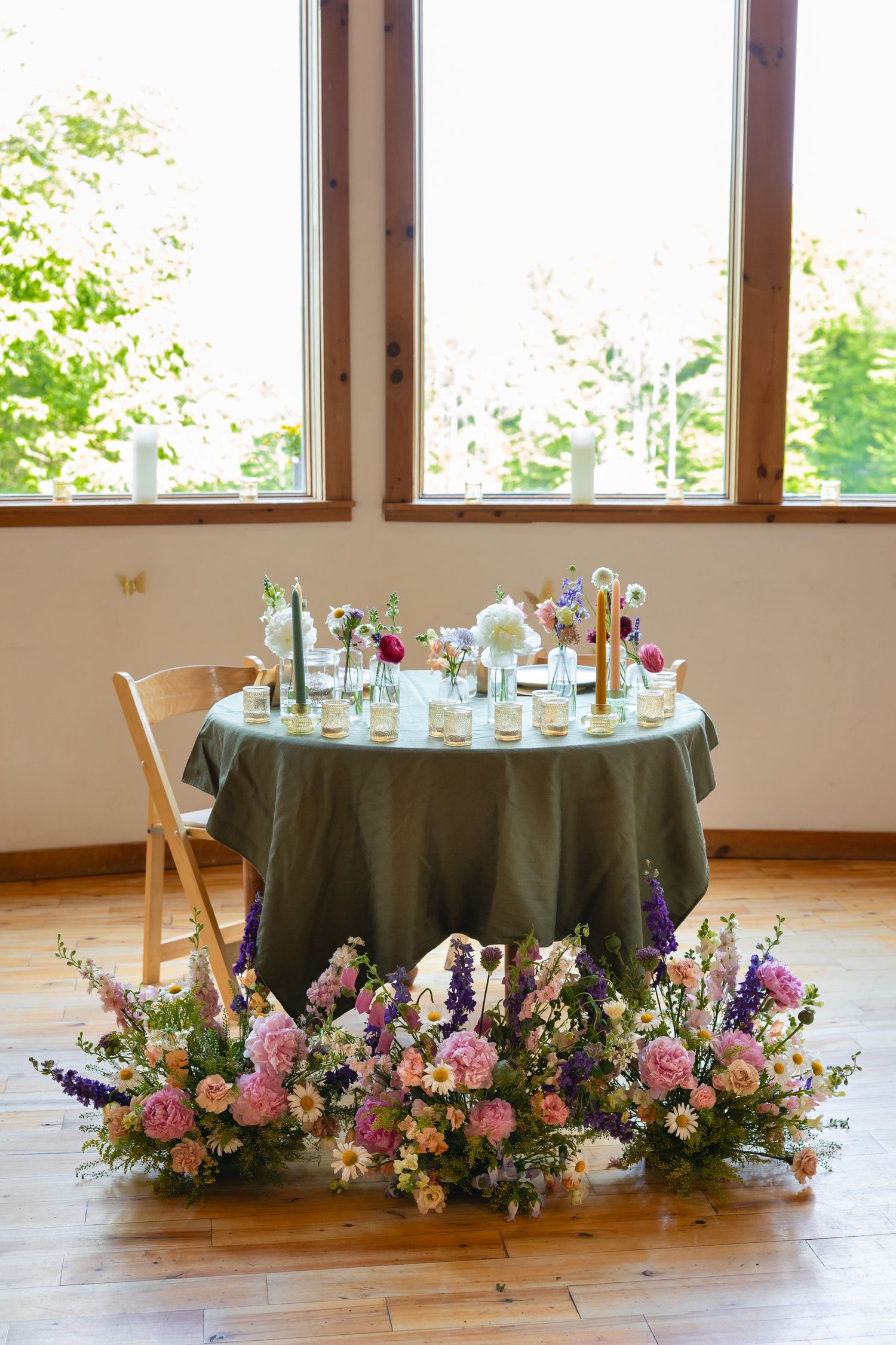 A round table with dark green tablecloth surrounded by floral arrangements of pink and purple flowers on a wooden floor.