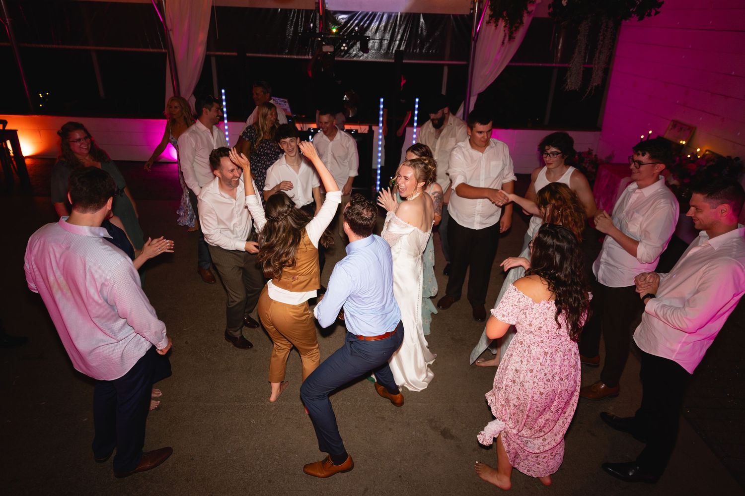 People dancing together in a dimly lit room with pink and purple lighting creating a festive atmosphere.