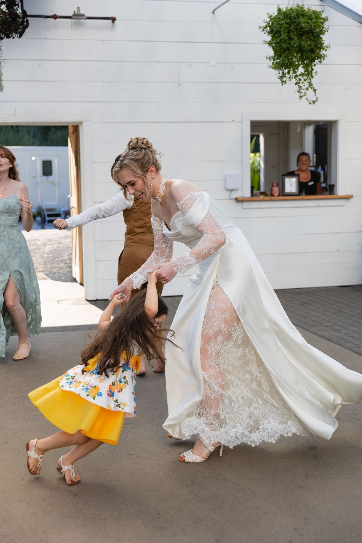 A playful dance sequence showing a bride in a lace dress twirling with a young girl in a yellow dress on a patio.