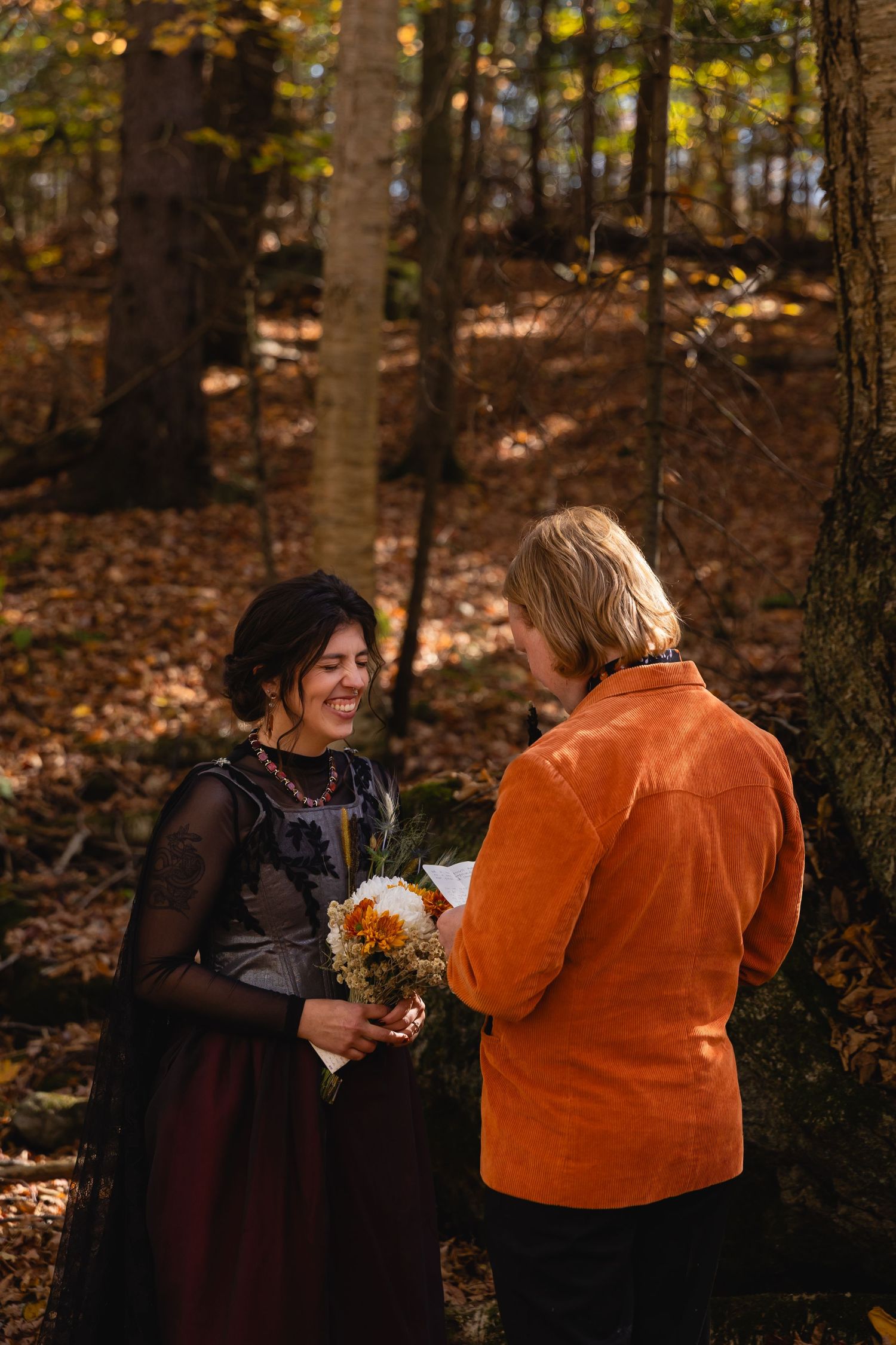 Two people share a joyful moment together in an autumn forest setting with fallen leaves and trees in the background.