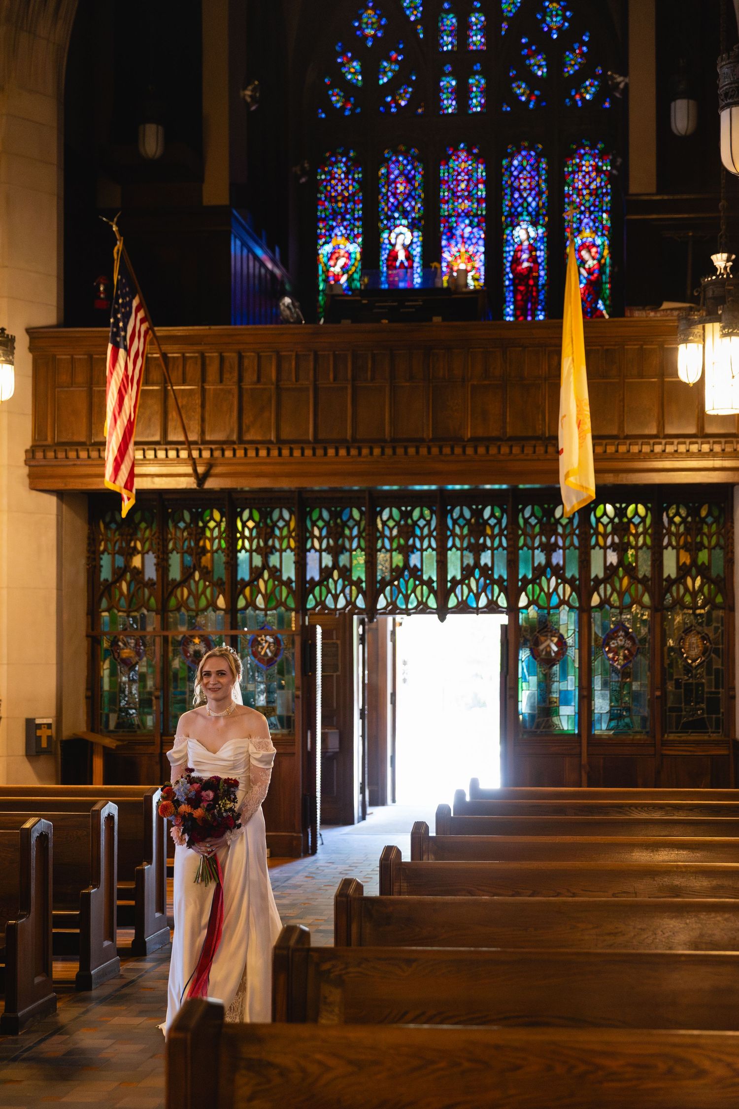 A wedding ceremony in a church with beautiful stained glass windows and wooden pews illuminated by natural light.