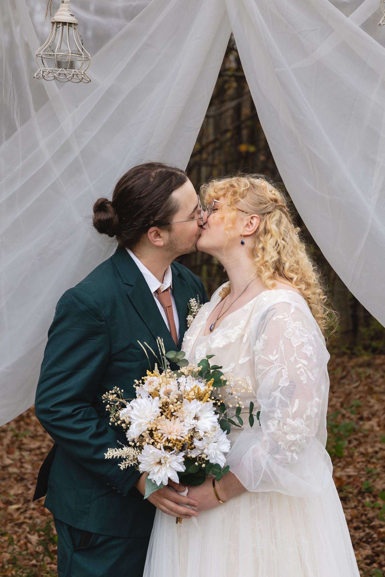 A romantic wedding moment under white drapery with a bouquet of white and gold flowers.