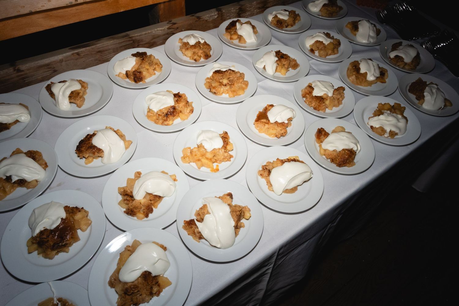 Multiple white plates arranged in rows on a table containing portions of dessert or pastry with brown and cream toppings.