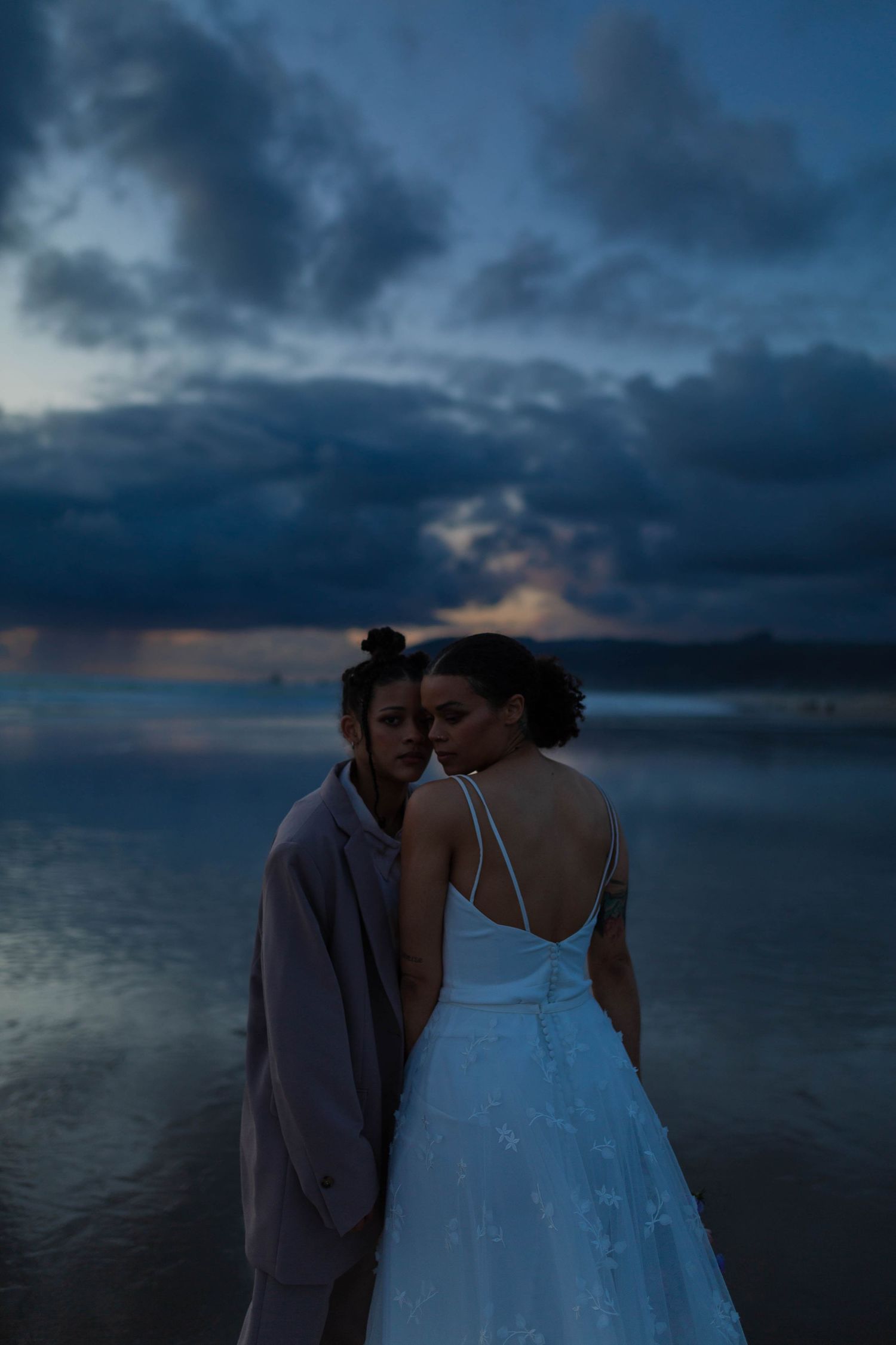 A romantic beach photo with a couple against moody blue storm clouds at sunset.