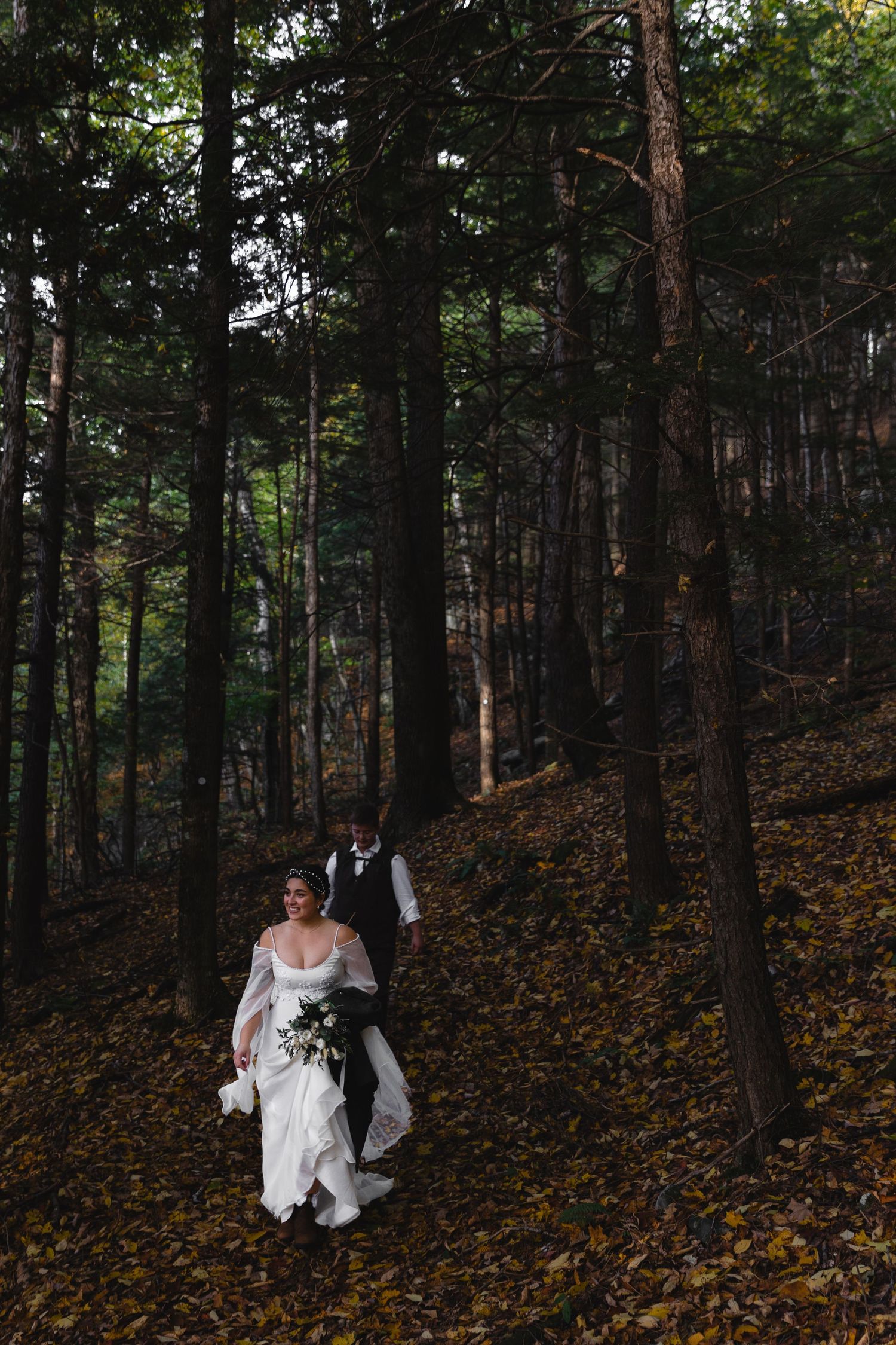 A couple descends a forest path covered in fallen autumn leaves.