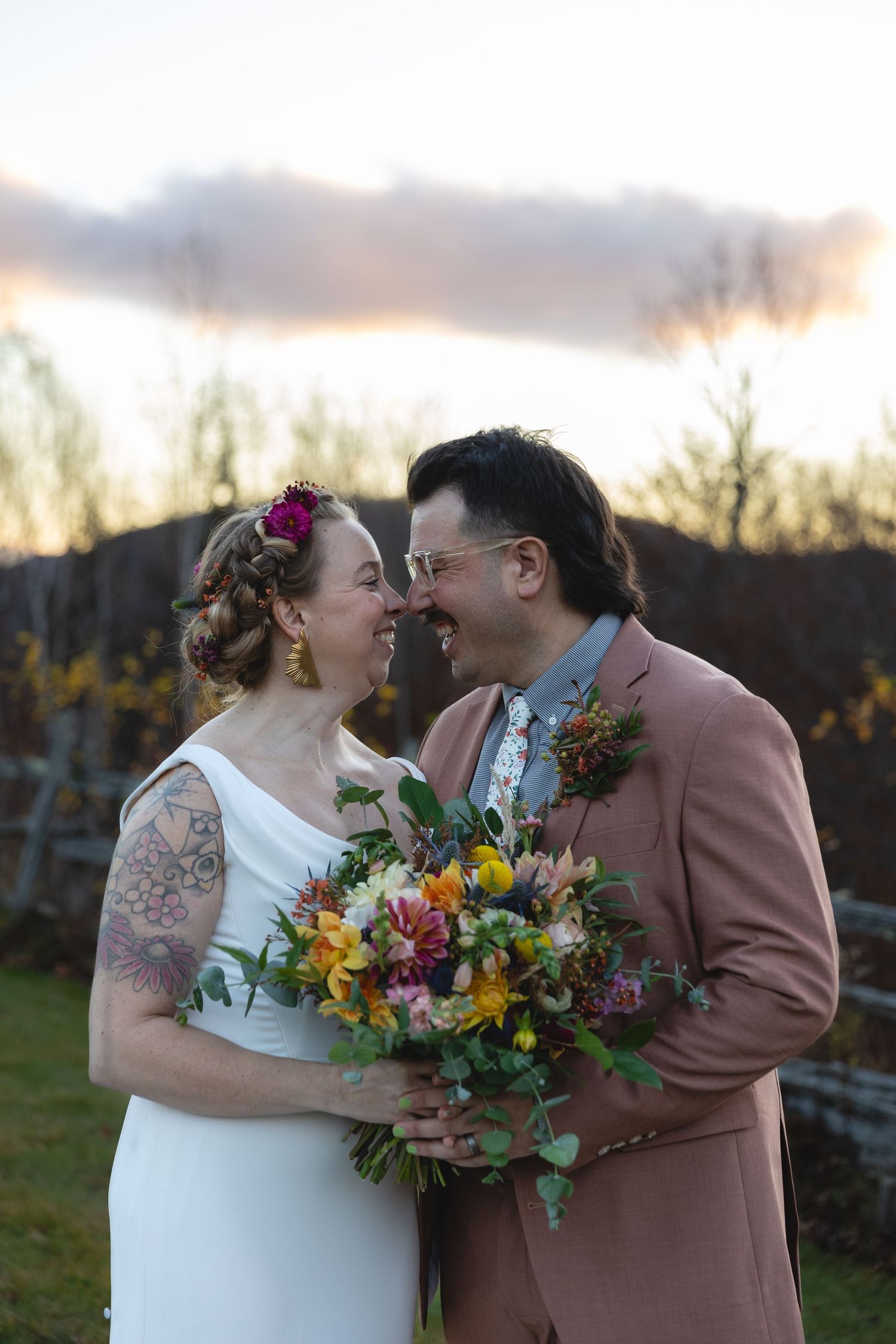 Wedding couple shares an intimate moment with vibrant fall bouquet at dusk.