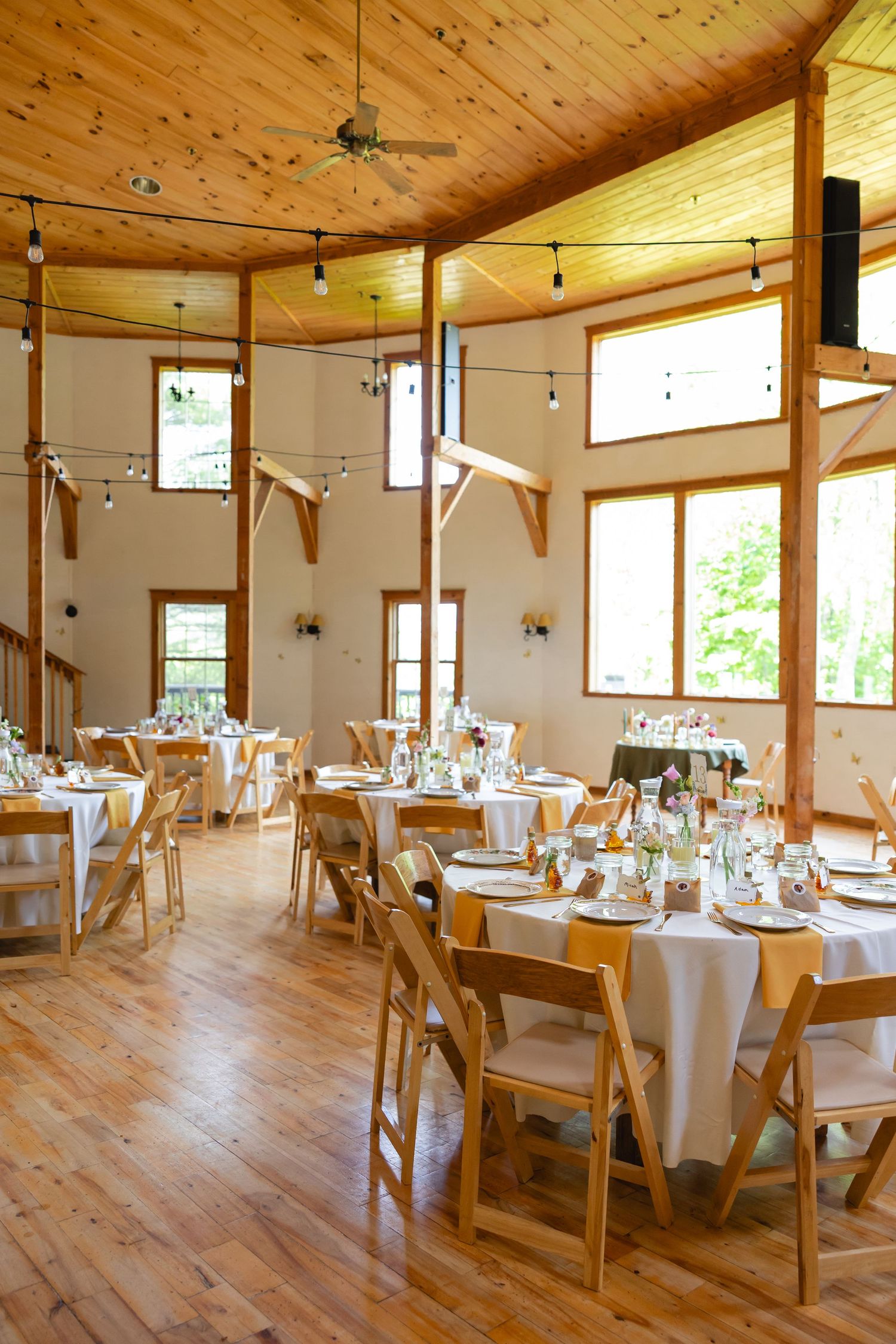 Rustic wedding reception venue with wooden ceiling, natural light, and round tables set with white linens and wooden chairs.