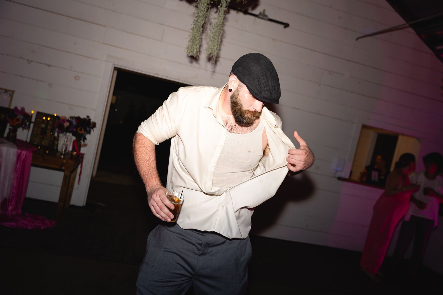 A person in a white shirt and baseball cap dances energetically in a dimly lit room with pink lighting.