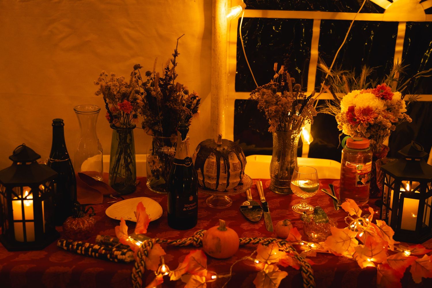 Glowing candles and string lights create a warm, romantic ambiance in an outdoor evening dining setting.