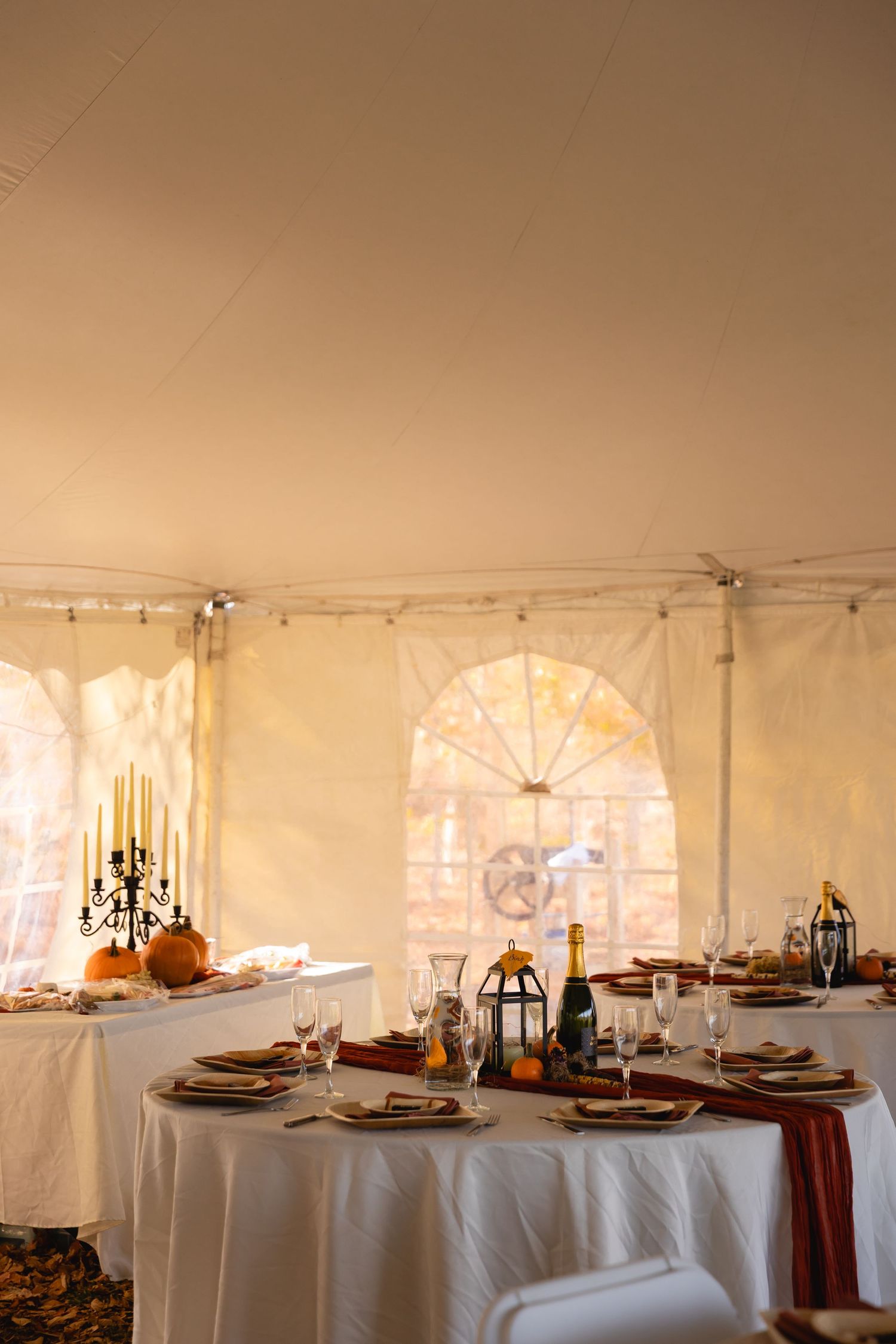White event tent interior with elegant round tables set for a formal dinner reception with autumn-themed decor and lighting.