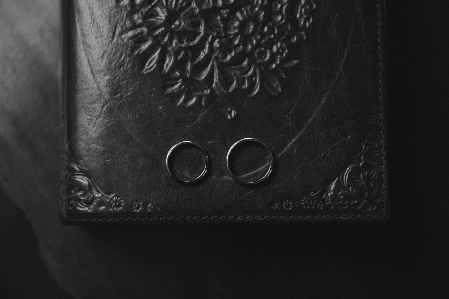Two wedding rings photographed on a dark textured surface in black and white.