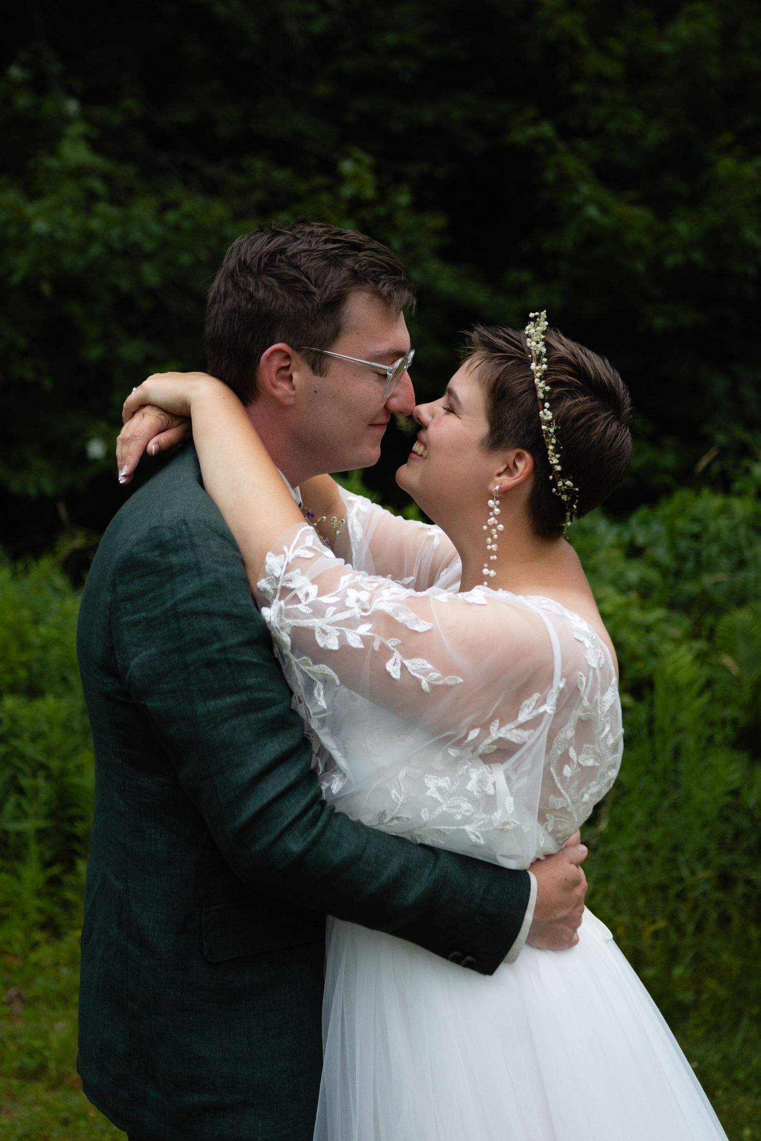 Romantic close-up of newlyweds embracing outdoors with lush greenery in background.