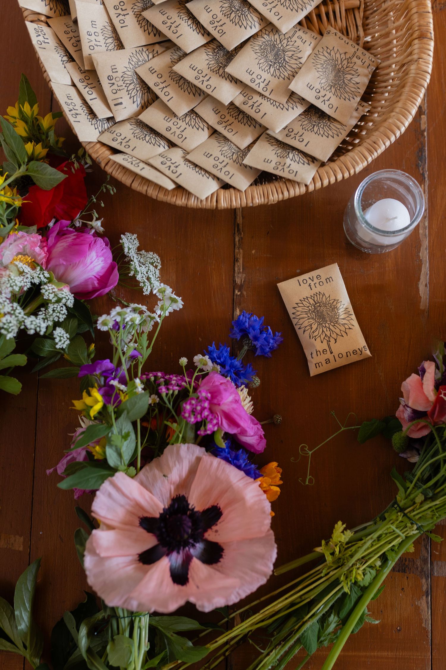 Colorful flower arrangement with pink poppy and seed packet collection in woven basket.