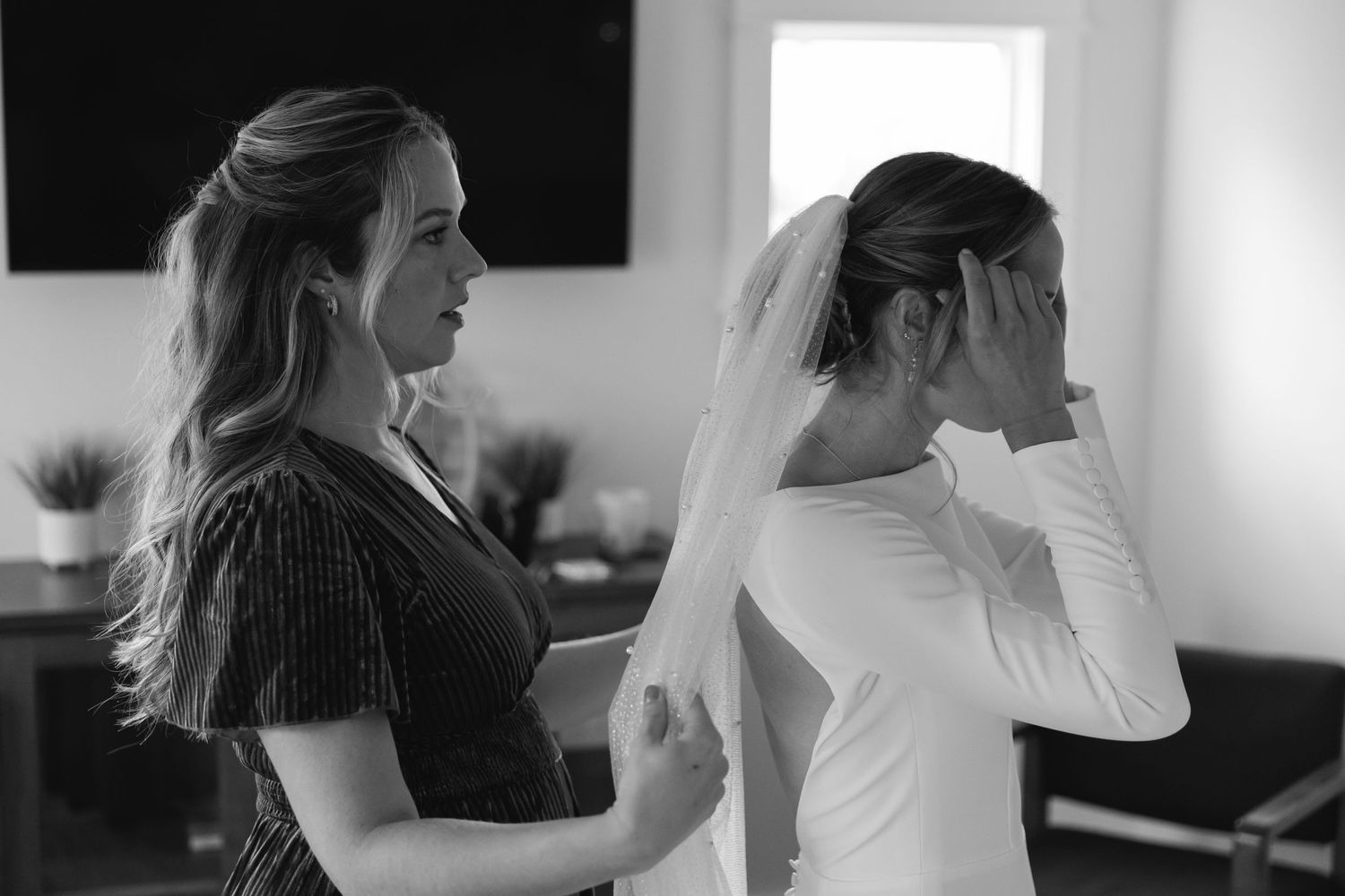 A black and white photo shows a bride in a white dress and veil with another person in dark clothing beside her.