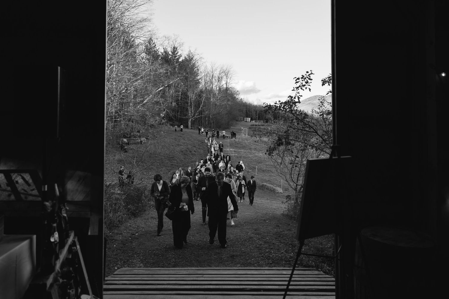 Black and white view through doorway of people walking along a rural path surrounded by trees.