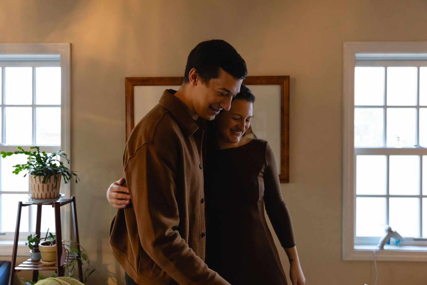 A couple shares an intimate moment together in a warmly lit room with sunlight streaming through windows.