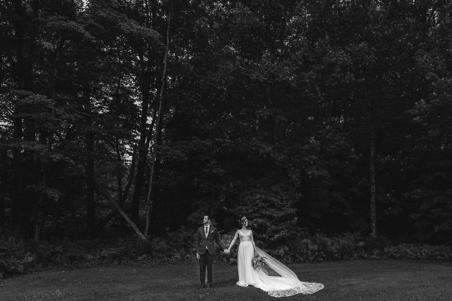 Black and white wedding portrait in woodland setting with flowing bridal veil.