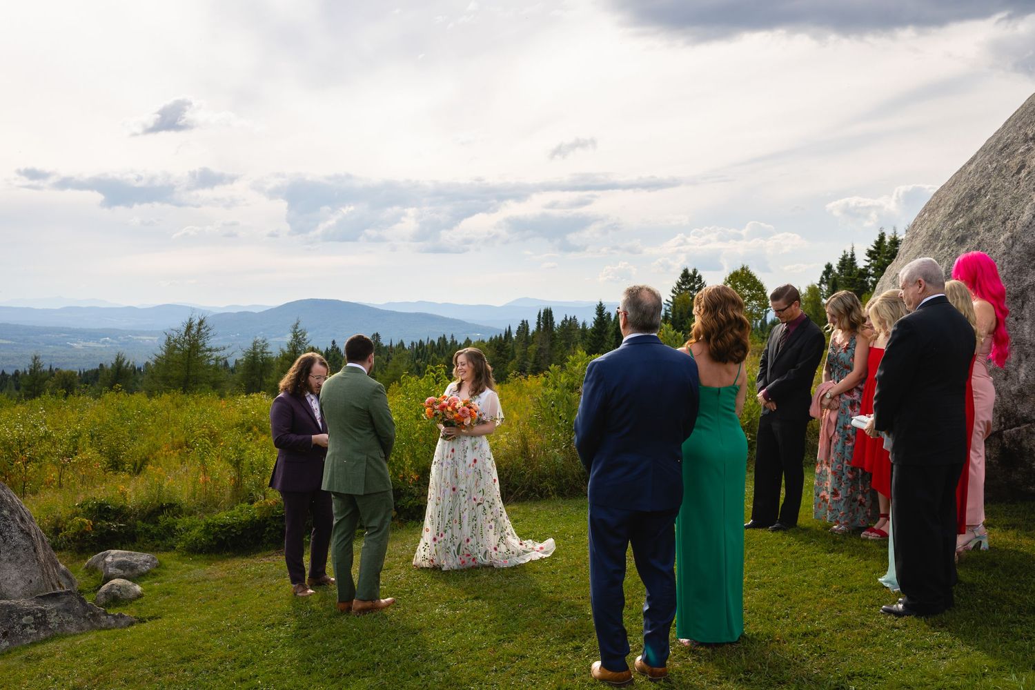 Small outdoor wedding ceremony on mountain summit with panoramic valley views under cloudy sky.