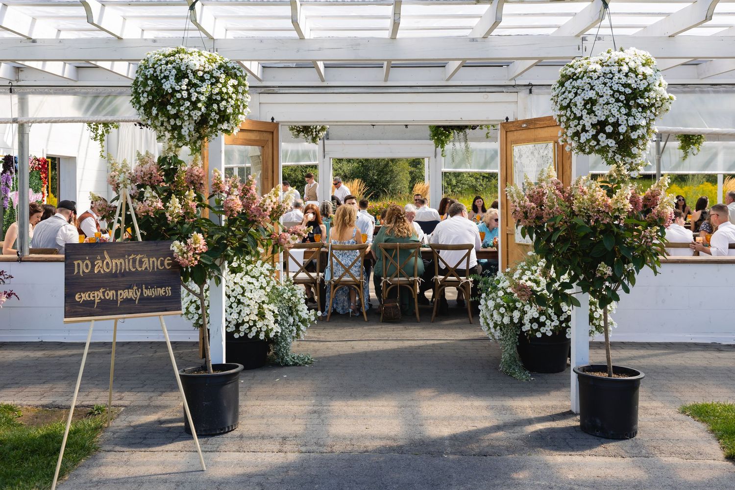 Elegant outdoor dining area with white pergola, hanging plants, and potted greenery creating a serene atmosphere.