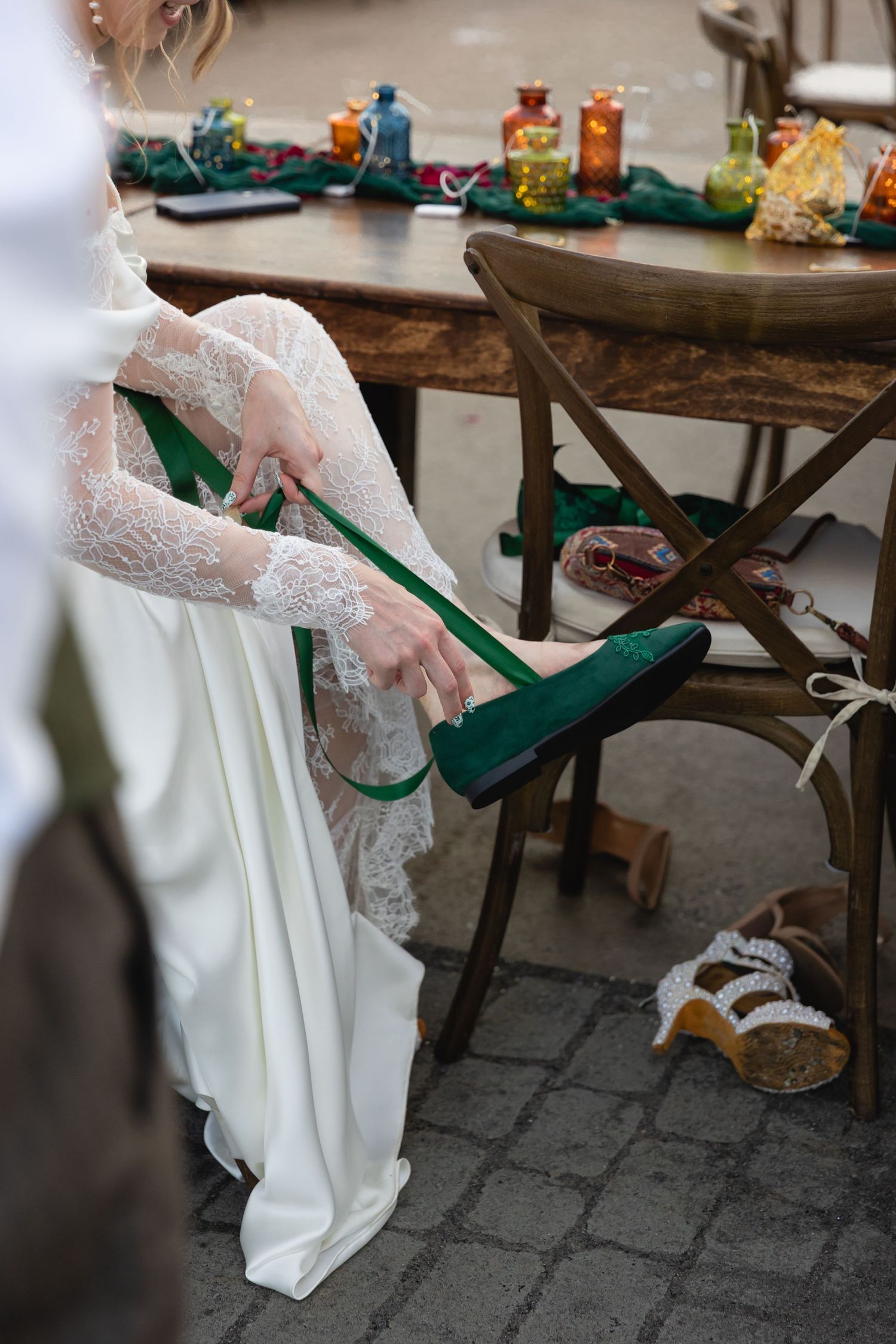 Close-up detail of white lace wedding dress with emerald green high heel shoes on rustic wooden surface.