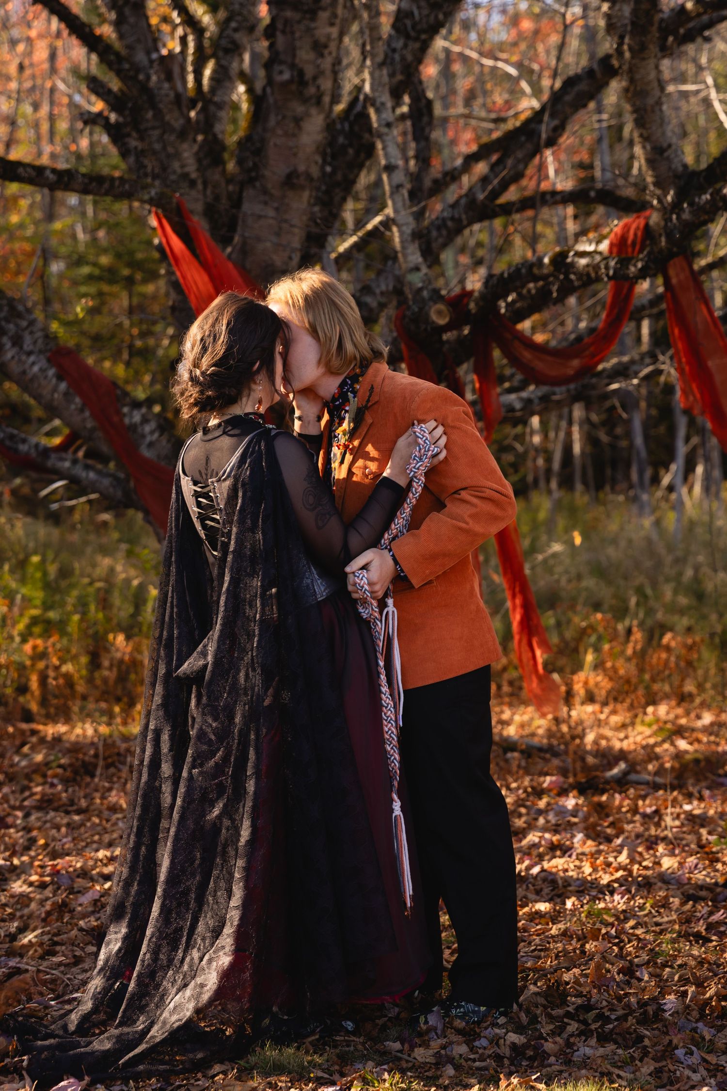 A couple shares a tender moment among autumn trees during an outdoor photoshoot in the golden afternoon light.