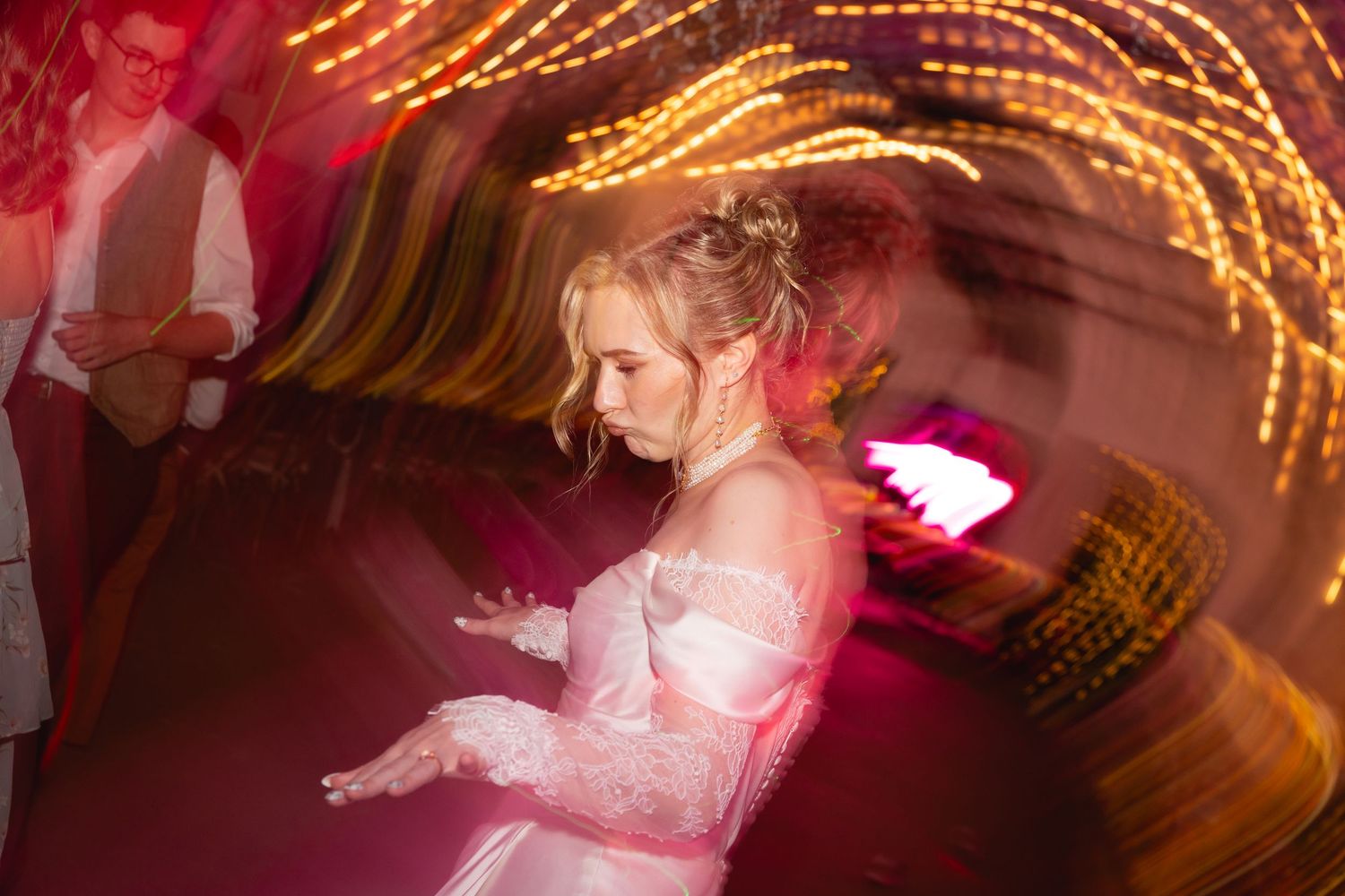 Motion-blurred photo of someone in a white formal dress dancing at an event with golden light trails in the background.