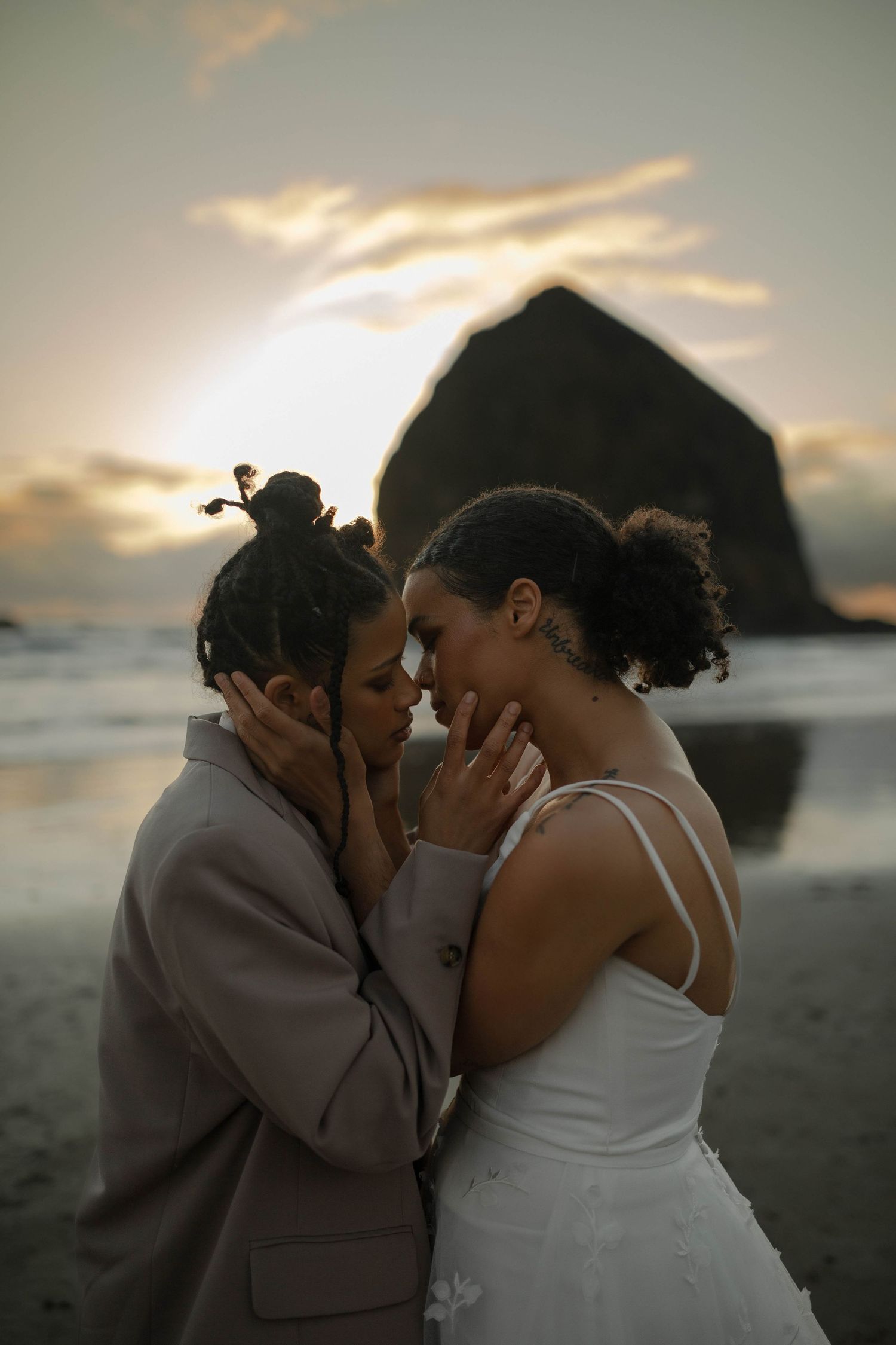 A romantic sunset wedding portrait with Haystack Rock creating a dramatic silhouette in the background.