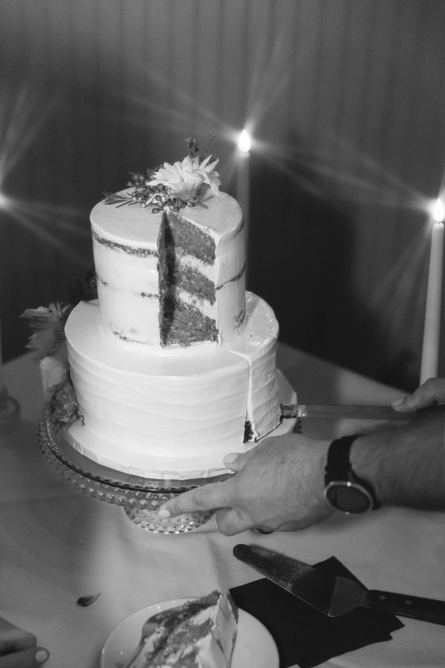 A black and white photo of a sliced wedding cake with sparkly decorations.