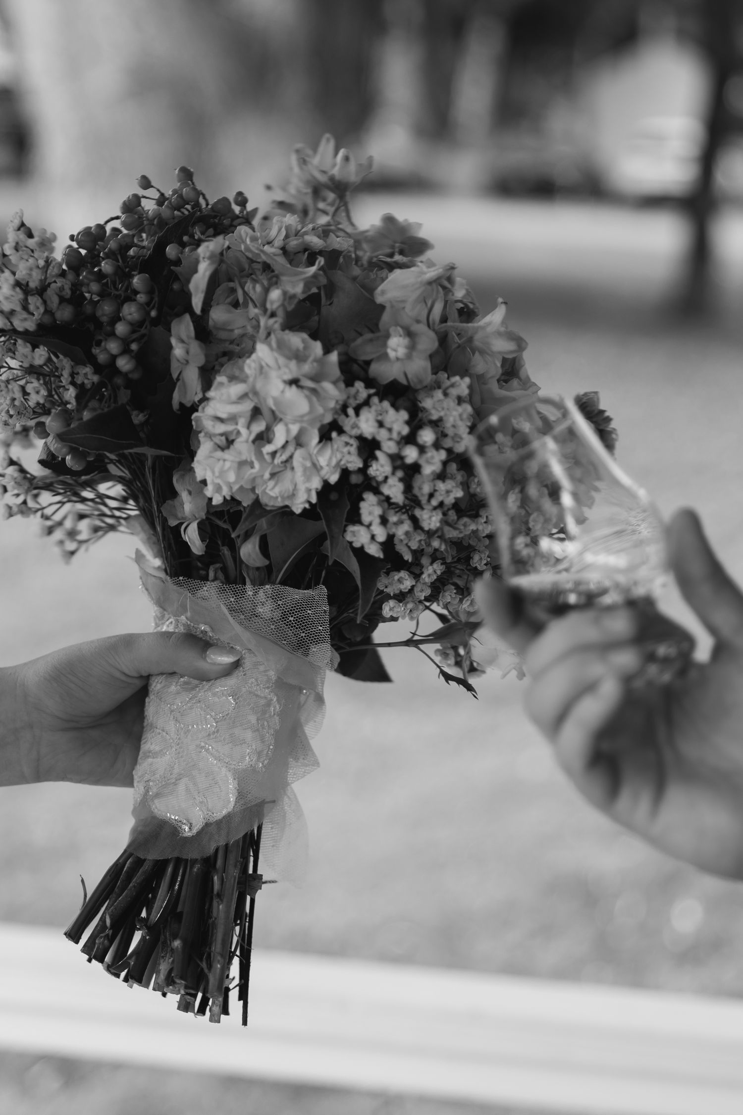 A black and white photograph shows hands holding a delicate bridal bouquet wrapped in lace ribbon.