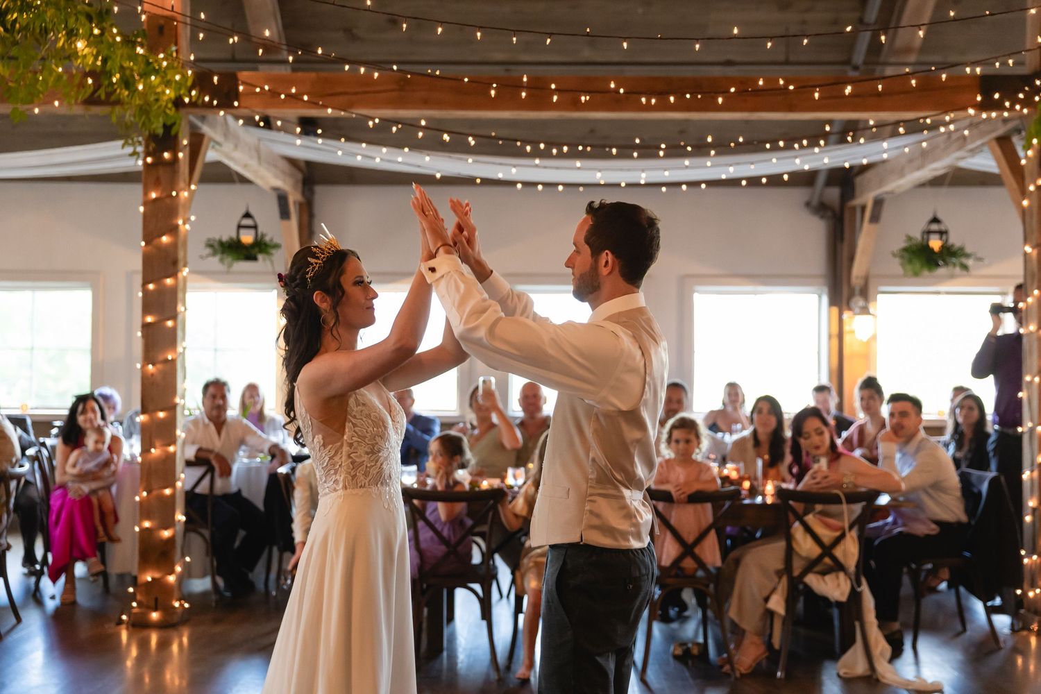 Couple dancing together in rustic reception hall decorated with twinkling lights.