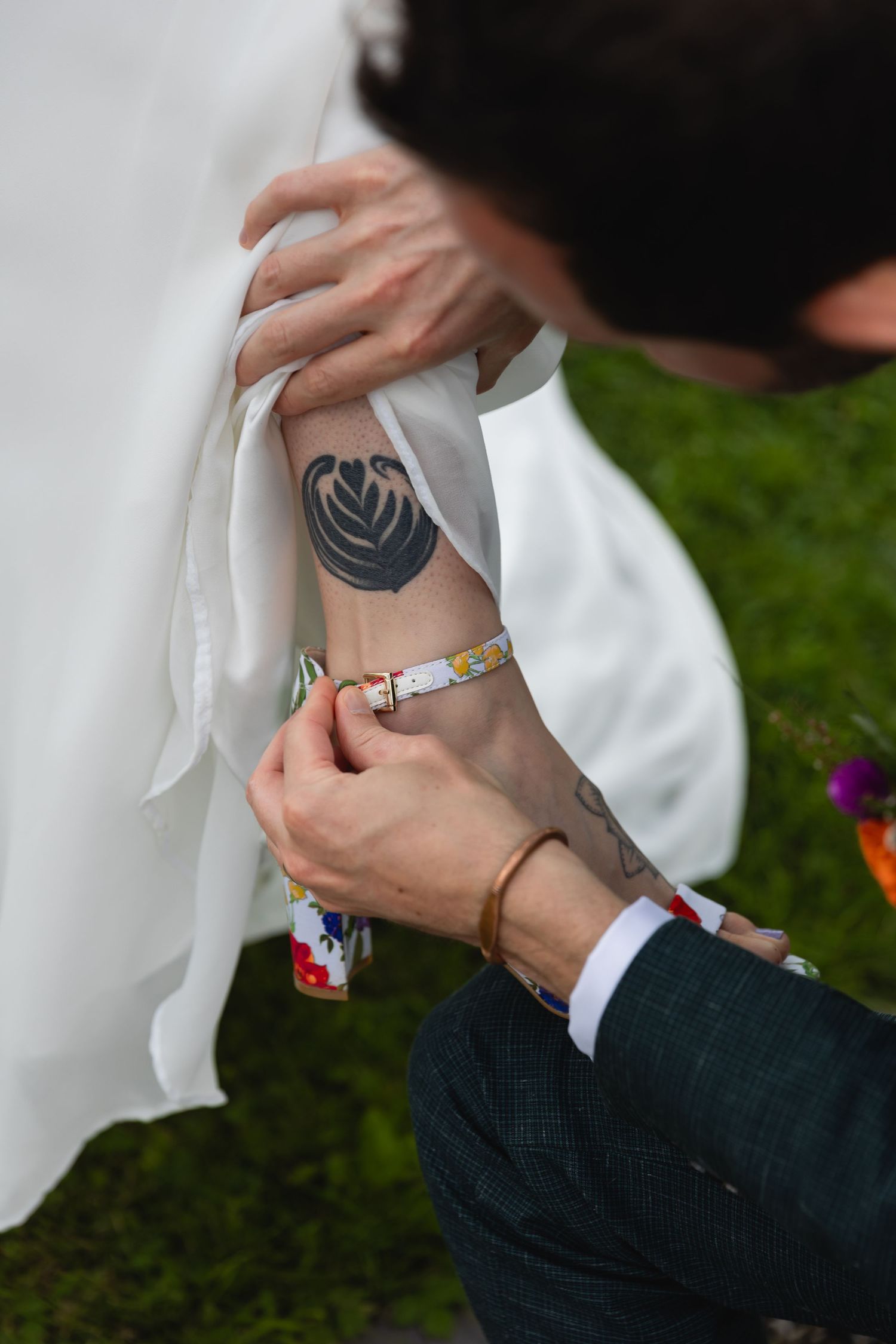 Close-up of hands revealing a heart-shaped tattoo and colorful bracelet against white fabric.