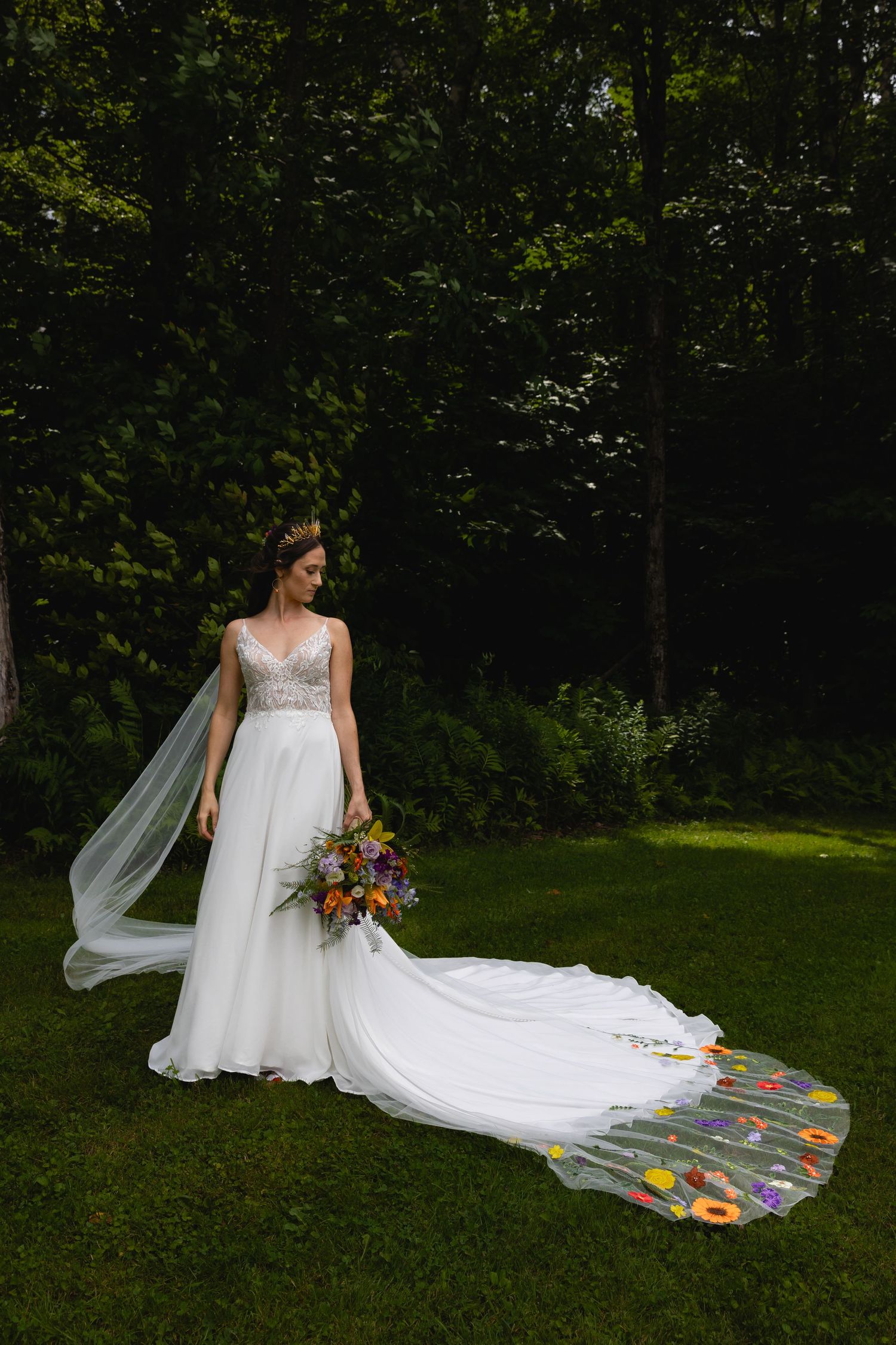 Elegant wedding dress with floral embroidered train and vibrant bouquet in an outdoor garden setting.