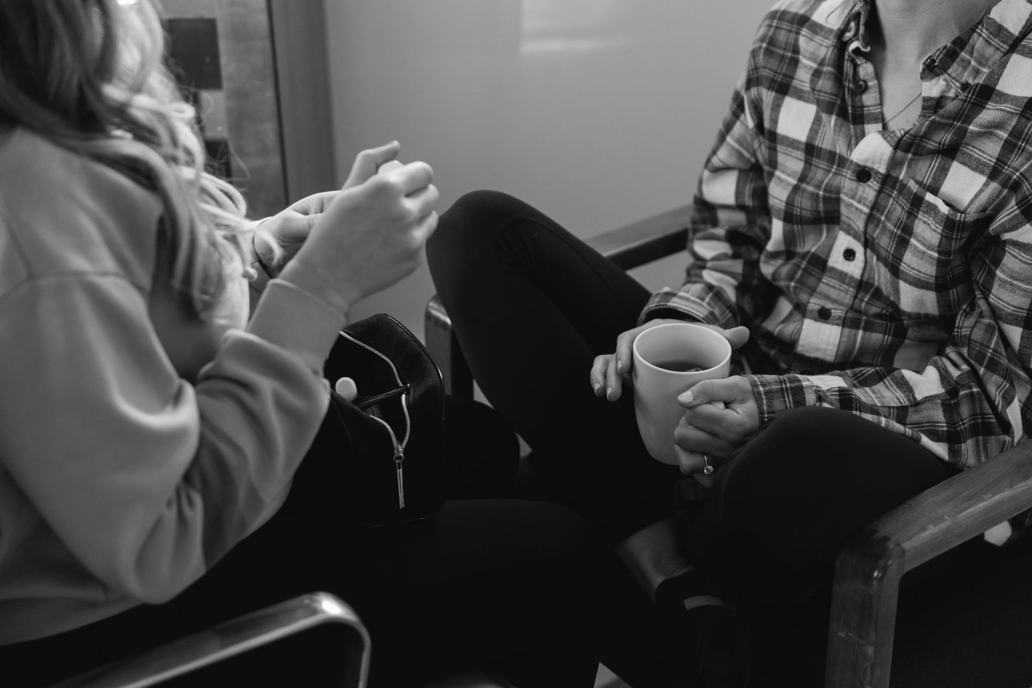 Black and white image showing two people sitting casually with coffee mugs in an indoor setting.
