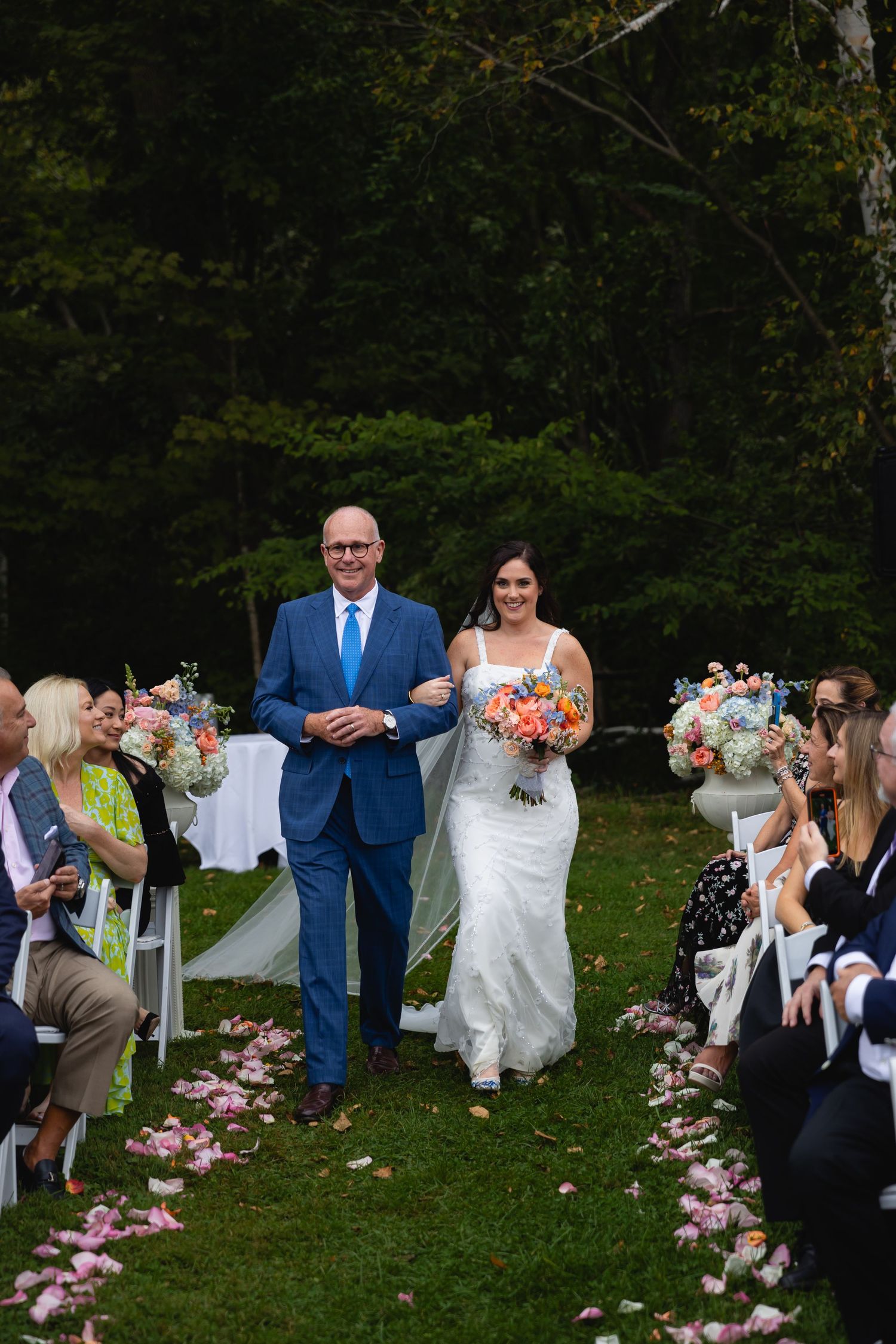 Outdoor wedding ceremony in a green garden setting with flower petals lining the aisle path.