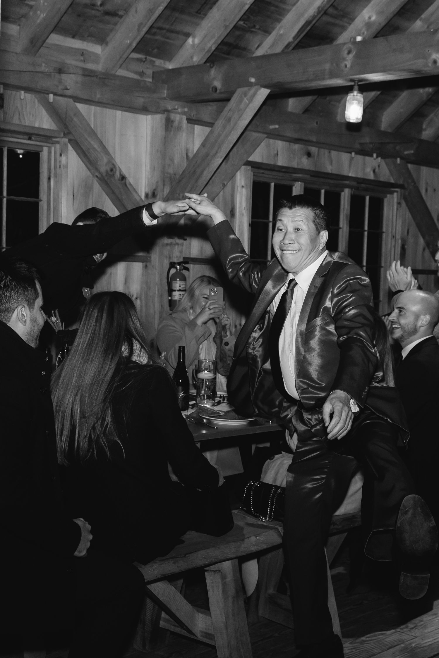 A lively party scene with people gathered inside a rustic wood-beamed room during what appears to be a social gathering.