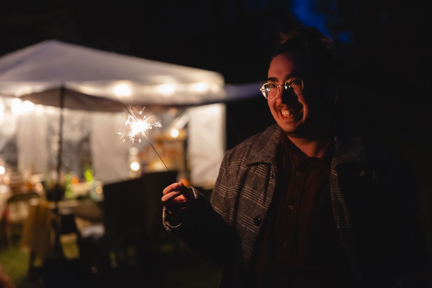 Person holding a sparkler in the dark while wearing glasses.