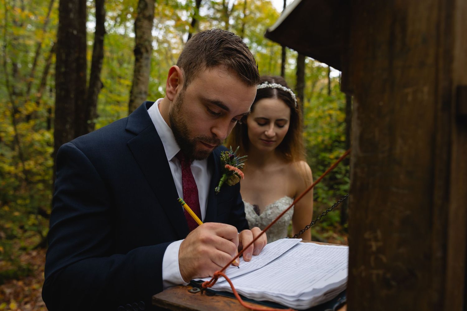 Couple signing wedding documents outdoors in autumn forest setting.