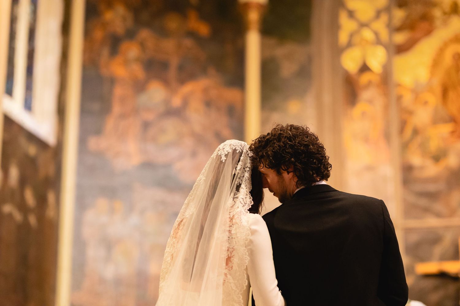 A couple shares an intimate moment at the altar during their wedding ceremony in a church with ornate wall murals.