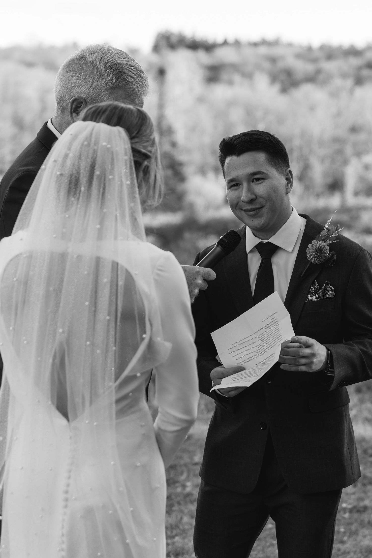 Black and white photo of a wedding ceremony showing couple exchanging vows outdoors with officiant present.