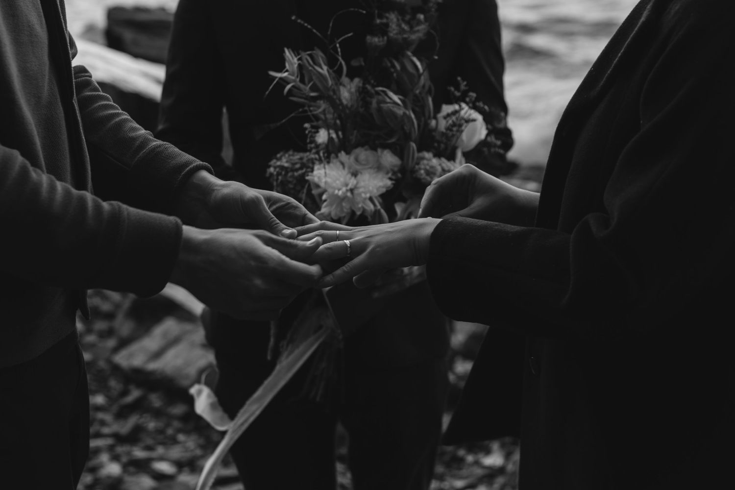 Two people holding hands together around a bouquet of flowers in a black and white photograph.
