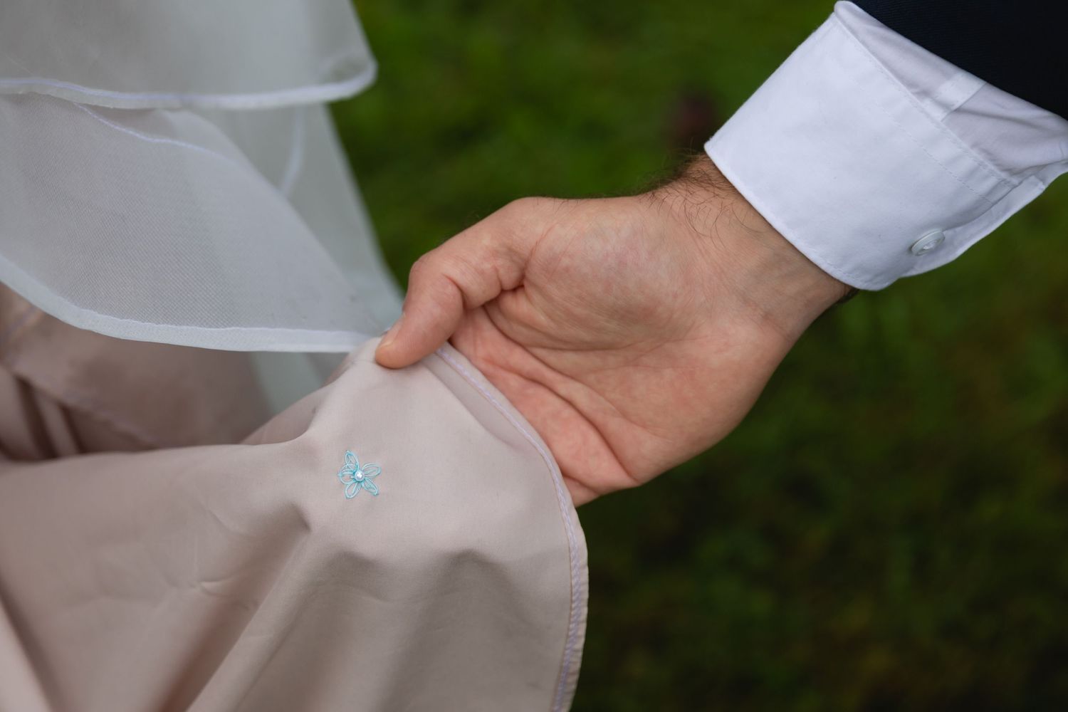 Close-up detail shot of hands adjusting wedding dress fabric outdoors.