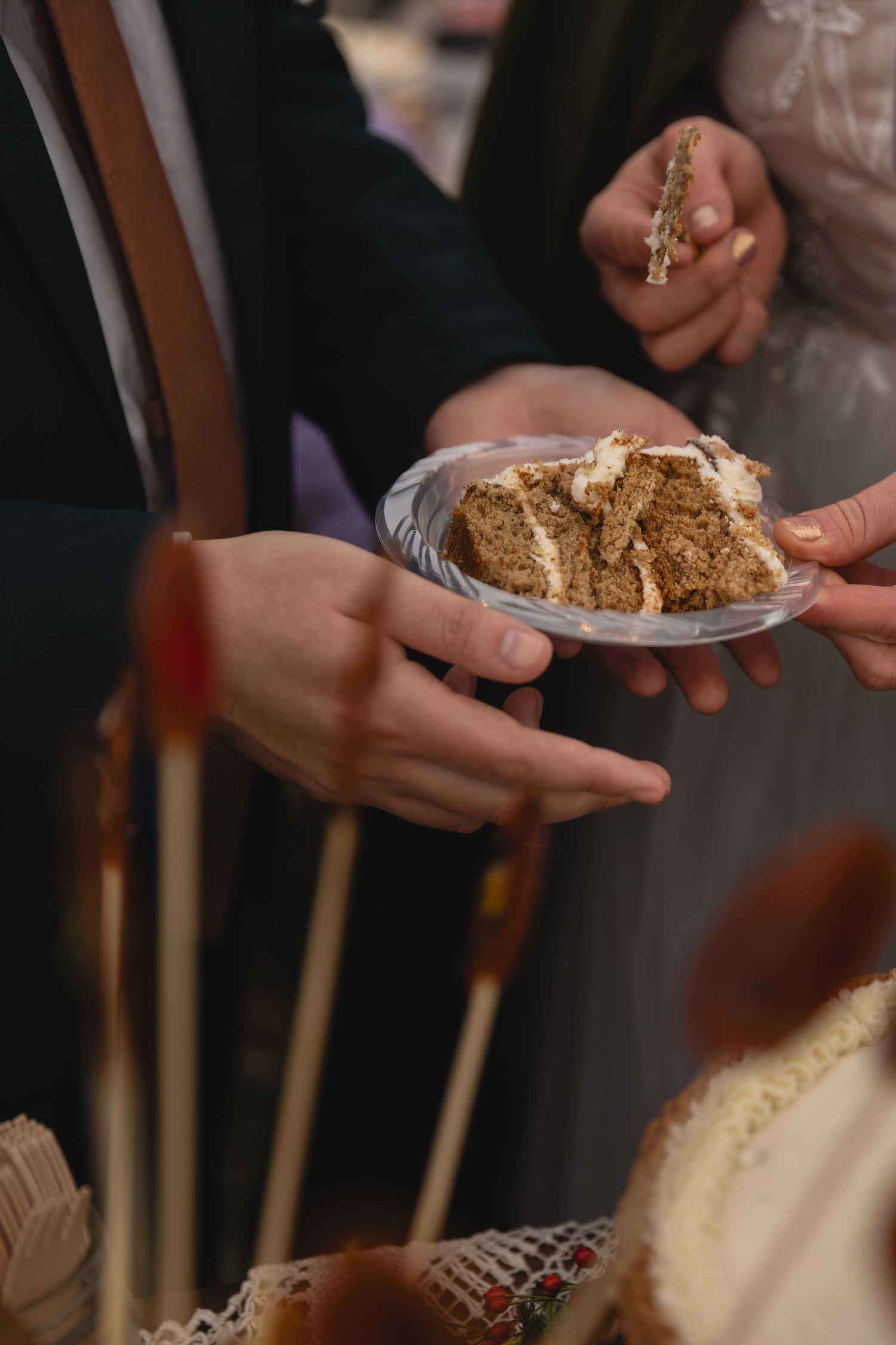 Hands sharing a slice of wedding cake during reception.